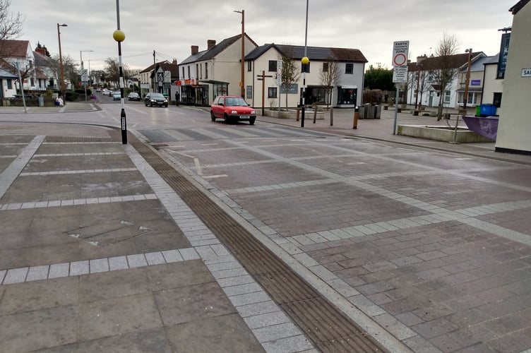 A car approaching the crossing on Sandy Lane, Caldicot with The Cross pub and Newport Road to the right.

