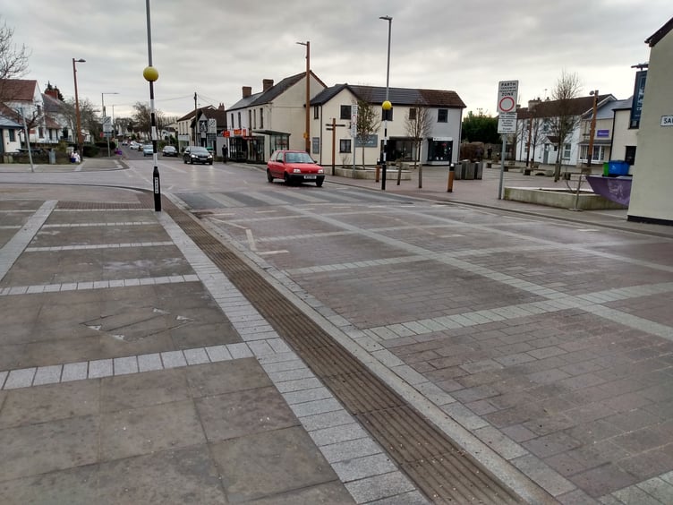 A car approaching the crossing on Sandy Lane, Caldicot with The Cross pub and Newport Road to the right.